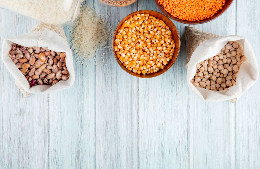 top view of different types of legumes and cereals kidney beans rice dried corns red lentils and chickpeas in sacks and bowls on rustic background with copy space