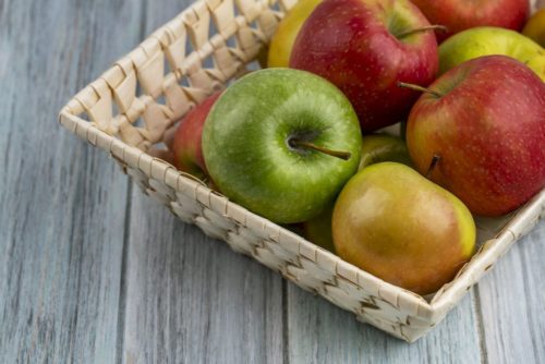 side view colored apples in a basket on a gray background